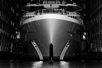 The imposing bow of a luxury yacht gleams under dramatic lighting within a dark shipyard.