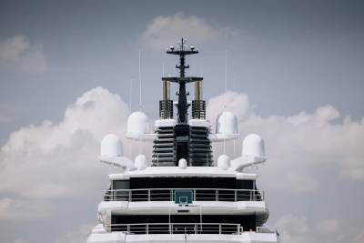 A modern superyacht's radar array and decks are framed by a dramatic cloudy sky.