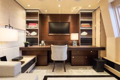A luxurious yacht cabin features a sleek wooden desk with a modern chair, flanked by illuminated shelving and a wall-mounted television.