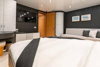 A luxurious yacht cabin features a large bed, a comfortable sofa, and modern entertainment amenities.