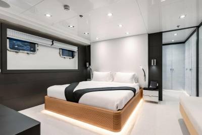 A modern yacht bedroom features a sleek platform bed with ambient lighting, complemented by porthole windows and a spacious closet.