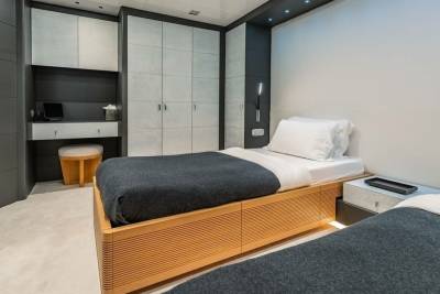 Two twin beds with dark grey blankets are neatly made in a modern, minimalist bedroom with ample storage.