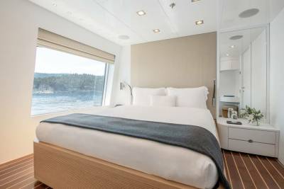 A modern bedroom with a large window offers stunning views of a tranquil body of water and lush green hills.