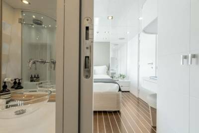 A modern yacht cabin features a sleek bathroom with a glass shower and a minimalist bedroom with a cozy bed.