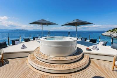 Luxurious yacht deck with a circular jacuzzi, plush loungers, and umbrellas offers a perfect oasis against a stunning ocean backdrop.