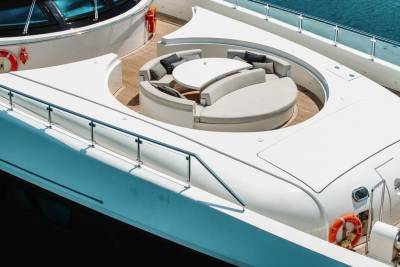 A luxurious yacht deck offers a circular seating area with plush cushions and a sleek table, perfect for enjoying the turquoise waters.