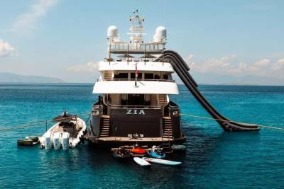 A luxurious yacht named Zia is anchored in crystal-clear turquoise waters, featuring an inflatable slide and various watercraft.
