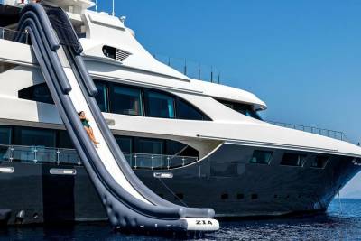 A woman in a green swimsuit slides down an inflatable yacht slide into the clear blue ocean.