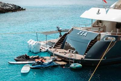 A luxurious yacht named Zia is anchored in crystal-clear turquoise waters, surrounded by jet skis and paddleboards.