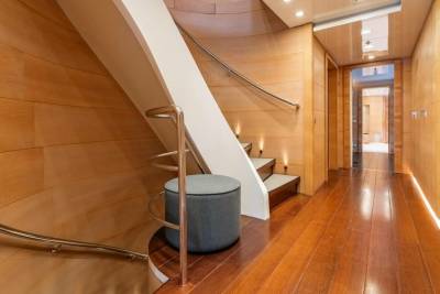 A modern yacht interior features a curved wooden staircase and a polished wooden hallway illuminated by soft lighting.