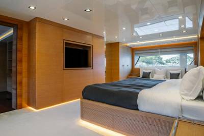 Luxurious yacht interiors feature warm wood paneling and a plush bed with a stunning ocean view.