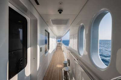 The sunlit deck of a luxurious yacht offers a serene walkway with ocean views through arched windows.