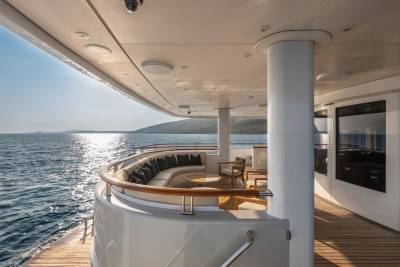 A luxurious yacht deck offers a comfortable seating area with ocean views and a sun-drenched coastline in the distance.
