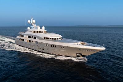 A sleek, modern superyacht glides through calm blue waters under a clear sky.