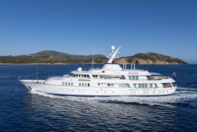 The majestic yacht Lady Beatrice glides through the deep blue waters under a clear sky, with rugged, tree-covered islands in the background.