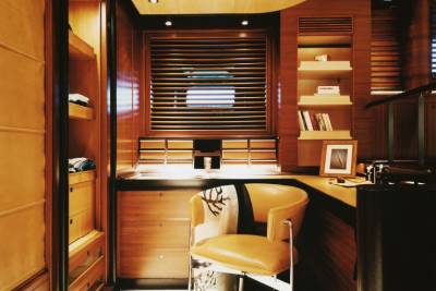 A stylish office space features warm wood tones, a comfortable leather chair, and a window with horizontal blinds.