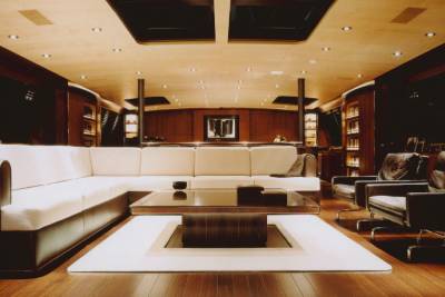 Luxurious yacht interior features a plush white sectional sofa, a modern coffee table, and dark leather armchairs.