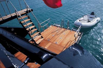 A luxurious yacht's teak deck and wooden stairs lead to the turquoise water where a tender awaits.