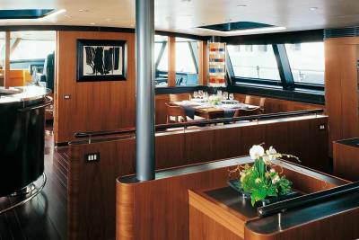 A luxurious yacht dining area features a polished wood interior, elegant table setting, and a striking modern artwork.