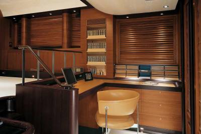 A luxurious yacht office features rich wood paneling, a sleek desk with a monitor, and a comfortable leather chair.