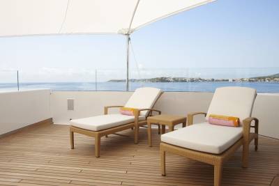Relax on a sun-drenched deck with a view of the sparkling Mediterranean Sea and a distant coastal city.