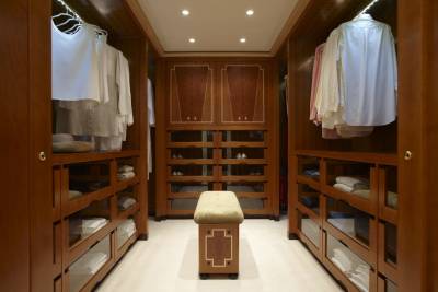 This luxurious walk-in closet features polished wood cabinetry, organized shelves, and a plush bench for a refined dressing experience.