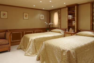 Luxurious twin beds with ornate gold patterned linens await in this elegant stateroom.