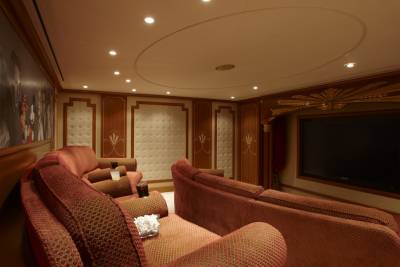 Luxurious red velvet theater seating faces a large screen, adorned with classic Hollywood murals and elegant wood paneling.