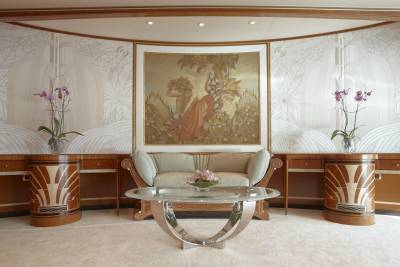 An opulent living space features a central sofa and coffee table beneath a classical painting, flanked by ornate desks and decorative wallpaper.