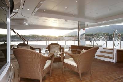 Relax in comfortable wicker chairs on a yacht deck overlooking a scenic coastline at sunset.