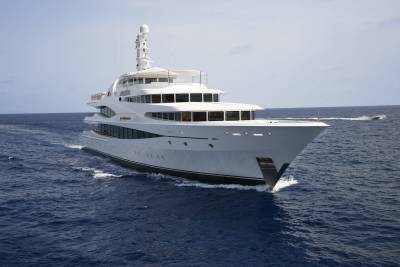 A luxurious white yacht glides through the deep blue ocean under a clear sky.