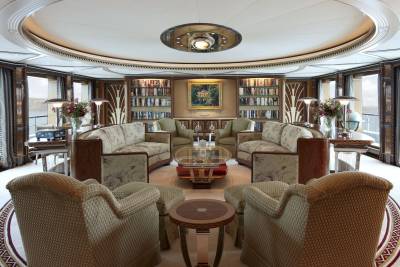 Luxurious yacht salon features plush seating, elegant bookshelves, and a central glass coffee table with a captivating painting above.