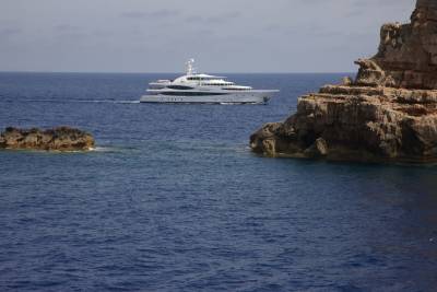 A luxurious white yacht glides through the deep blue ocean past rugged, rocky cliffs.