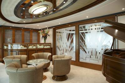 Luxurious lounge area with ornate display cabinets, comfortable seating, and a grand piano, all under a decorative ceiling.