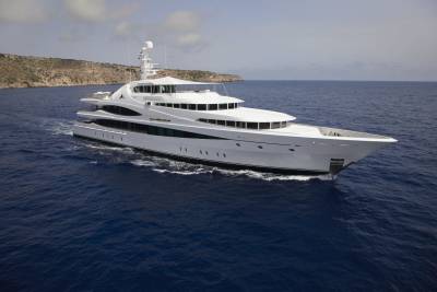 A luxurious white yacht glides through the deep blue ocean near a rocky coastline under a cloudy sky.