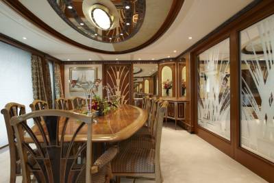 Elegant dining room aboard a luxury yacht features a polished wood table, ornate chairs, and decorative glass panels.