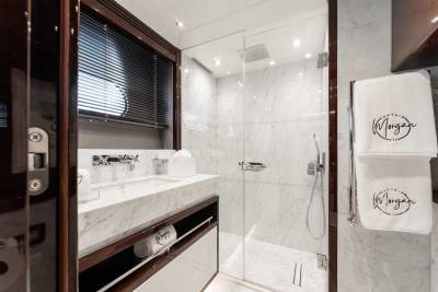 A modern, minimalist bathroom with a marble vanity, a glass shower enclosure, and towels with a logo on them.