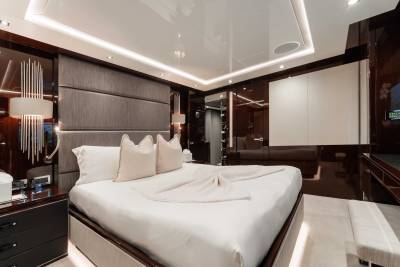 A modern and luxurious bedroom with a large, comfortable-looking bed, dark wood furniture, and recessed lighting in the ceiling creating a warm and inviting atmosphere.
