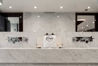 A marble countertop with various bathroom accessories, including a white towel with a logo, set against a backdrop of a marble wall with recessed lighting.
