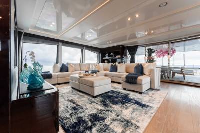 A spacious and elegantly furnished living room with a large sectional sofa, a patterned rug, and a glass-enclosed patio offering a scenic outdoor view.