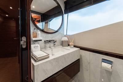 A modern and stylish bathroom with a large circular mirror, a marble vanity, and a window providing natural light.