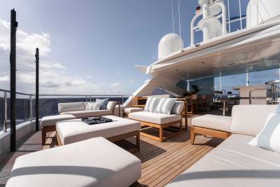 A luxurious outdoor seating area on the deck of a large yacht, with comfortable white furniture and a panoramic view of the ocean and sky in the background.