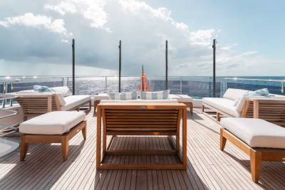 A wooden deck with comfortable outdoor furniture overlooks a vast expanse of ocean and cloudy sky.