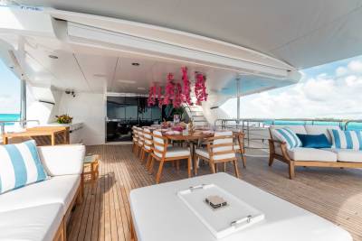 A luxurious yacht deck with a dining area, comfortable seating, and a stunning ocean view in the background.