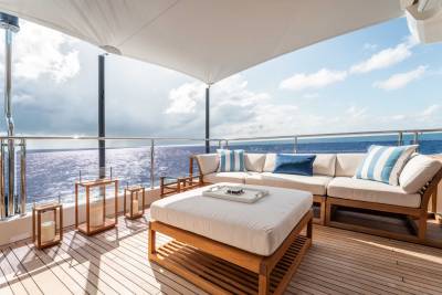 A cozy outdoor seating area on a ship's deck, with a comfortable sofa and ottoman overlooking the vast ocean and cloudy sky.