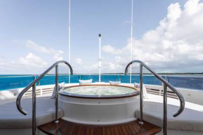 A white circular hot tub with metal railings on the deck of a boat, surrounded by a vast expanse of blue water and cloudy sky.