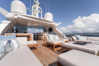 A luxurious yacht deck with comfortable seating arrangements, surrounded by a clear blue sky and fluffy white clouds.