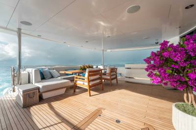 A spacious and luxurious outdoor deck overlooking a serene ocean view, adorned with comfortable seating, a vibrant floral arrangement, and a wooden floor that extends to the edge of the deck.