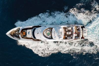 A large, luxurious yacht navigates through the choppy, dark blue waters, surrounded by a dramatic, rocky coastline.