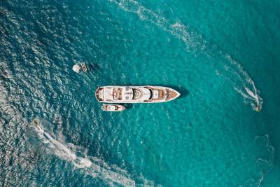 A luxurious yacht and its tenders bask in the vibrant turquoise waters, with jet skiers adding a splash of excitement.